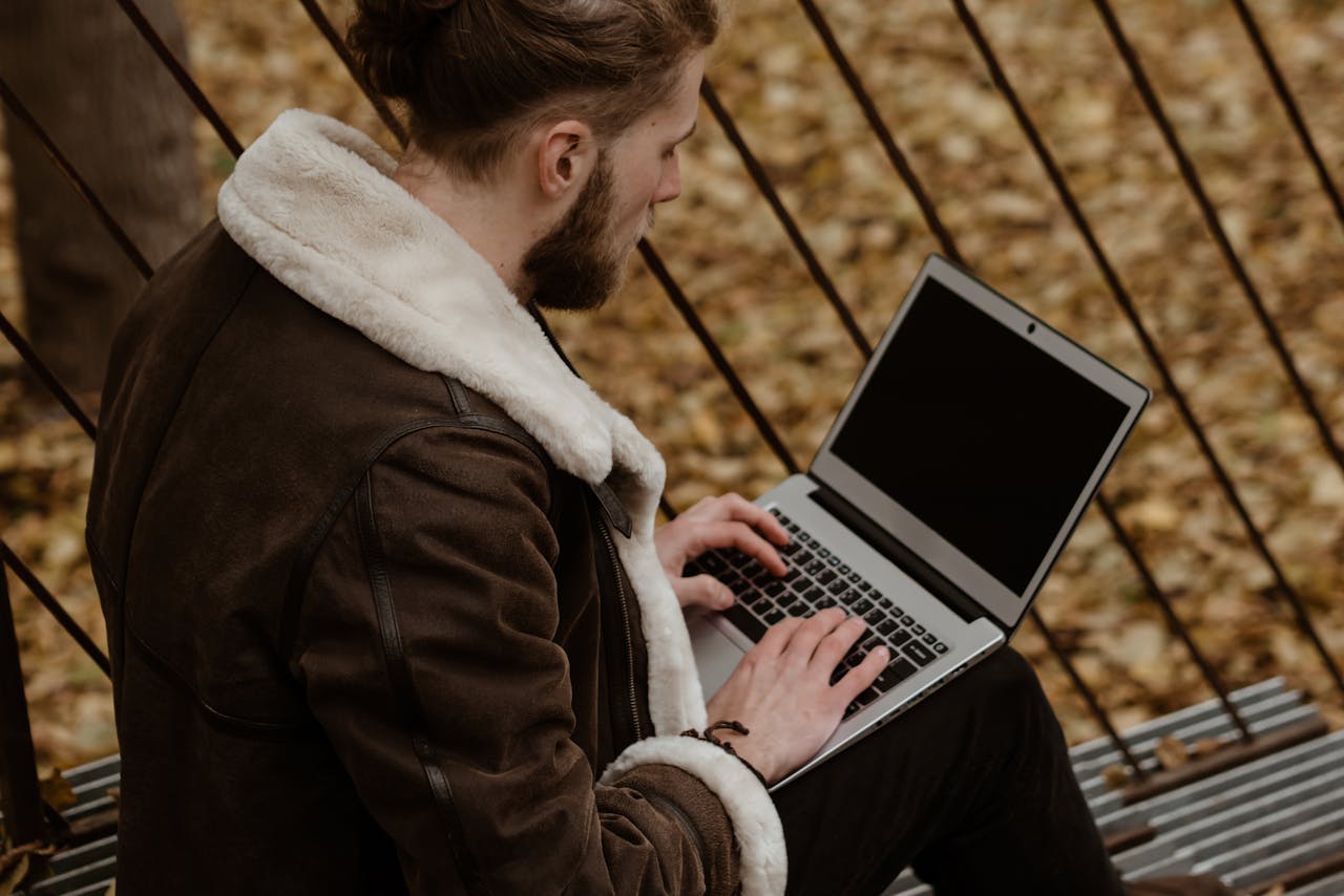 Man using a laptop outdoors in an autumn park, showcasing remote work lifestyle.